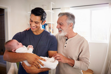 Proud Hispanic father holding his four month old son at home, grandfather standing beside them