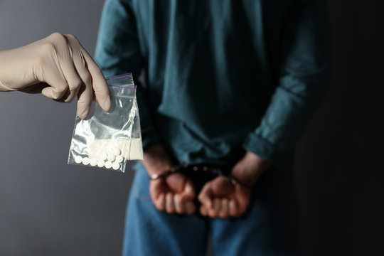 Police worker holding drugs in plastic bags near arrested dealer on color background