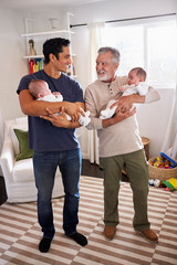 Young Hispanic man and his senior father holding his two baby boys at home, vertical