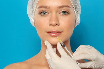 Young woman getting lips injection on color background. Cosmetic surgery