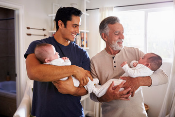 Young Hispanic man and his senior father holding his two baby boys at home