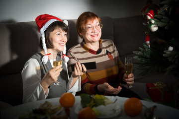 Happy mother and daughter drink champagne and watch TV on Christmas night