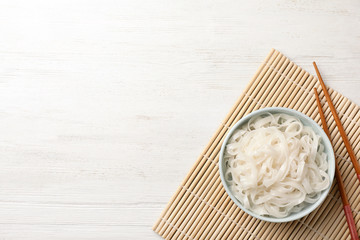 Bowl with rice noodles on wooden table, top view. Space for text