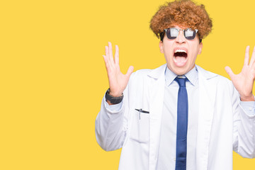 Young handsome scientist man wearing professional coat and sunglasses celebrating crazy and amazed for success with arms raised and open eyes screaming excited. Winner concept