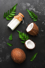 Fototapeta na wymiar Coconut and milk in a bottle on a dark stone background decorated with fern leaves. Top view, flat lay.