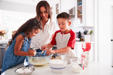 Brother and sister making cake mixture together at the kitchen table with their mum, waist up