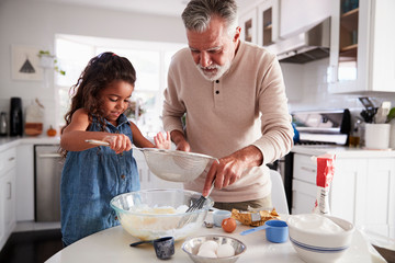 Young girl preparing cake mixture with her grandfather at the kitchen table, close up - Powered by Adobe