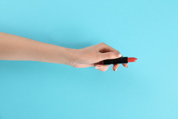 Woman holding lipstick on color background, closeup