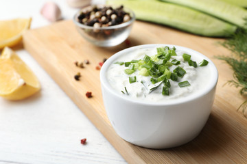 Ceramic bowl of cucumber sauce with ingredients on wooden table, space for text. Traditional Tzatziki