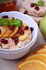 Porridge with caramelized apples and dried cranberries topped with mint surrounded by breakfast ingredients