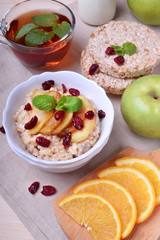 Porridge with caramelized apples and dried cranberries topped with mint surrounded by breakfast ingredients