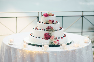 A beautiful wedding cake in four levels is on the table against the background of the picturesque lake