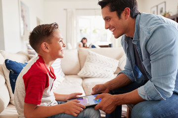 Fototapeta premium Pre-teen boy and dad playing a game on a tablet computer in the sitting room, close up