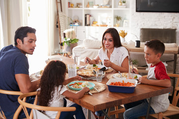 Young Hispanic family sitting at dining table eating dinner together