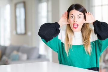 Young beautiful woman wearing winter sweater at home Trying to hear both hands on ear gesture, curious for gossip. Hearing problem, deaf