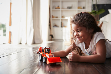 Young Hispanic girl lying on the floor in the sitting room playing with a toy digger truck