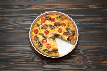 Baked homemade quiche pie in ceramic baking form on concrete background