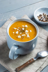Spicy pumpkin and sweet potatoes soup in big ceramic mug garnished with feta cheese.