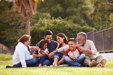 Happy three generation Hispanic family sitting on the grass together in the park, selective focus