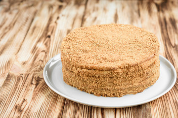 Homemade sweet layered honey cake with nuts on white plate on wooden table with bowl of honey, cinammon and badian.