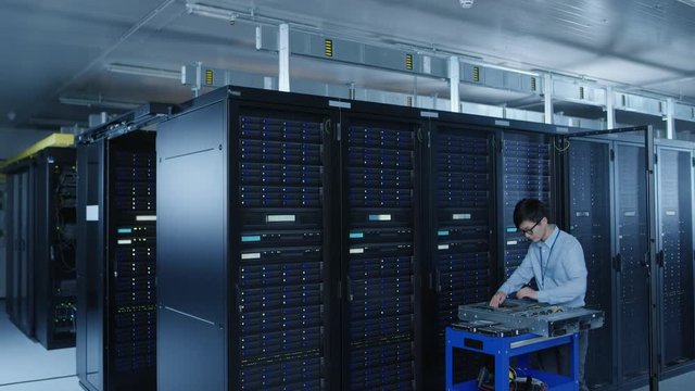 In the Modern Data Center: IT Technician Working with Server Racks, on a Pushcart Various Equipment Needed for Installing New Hard Drives, Doing Hardware Maintenance and Diagnostics.