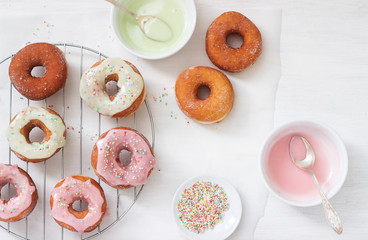 Homemade donuts decorated with colored icing and colored sugar on a light background.