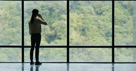 Fototapeta na wymiar Woman talk to cellphone over glass of window with green tree background