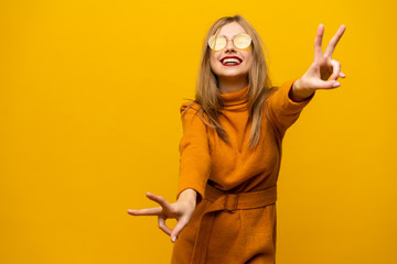 Image of happy young woman standing isolated over yellow background showing peace gesture. Looking camera