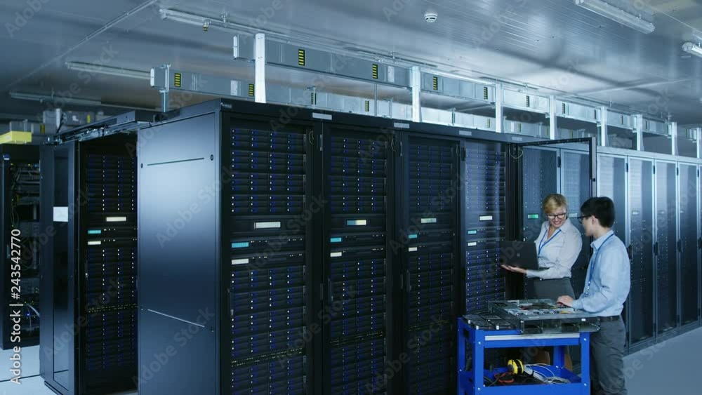 Leinwandbilder In the Modern Data Center: IT Technician Working with Server Racks, Pushes Cart Between Rows of Server Racks. On a Pushcart New Hardware for System Update. Engineer Doing Maintenance and Diagnostics.