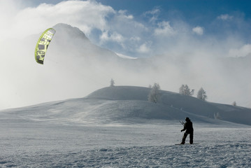 man who practices snowkite in the snow, with snowboard and kite on a windy day, fog, clouds and sun after a snowfall, mountain, alps, winter, outdoor, Simplon Pass, Switzerlan