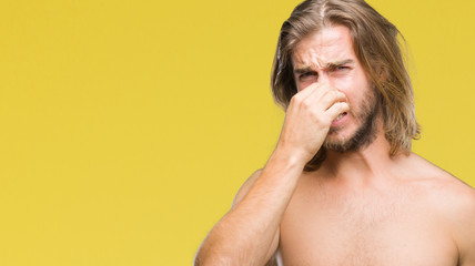 Obraz premium Young handsome shirtless man with long hair showing sexy body over isolated background smelling something stinky and disgusting, intolerable smell, holding breath with fingers on nose