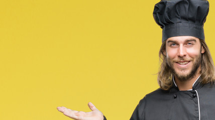 Young handsome cook man with long hair over isolated background smiling cheerful presenting and pointing with palm of hand looking at the camera.