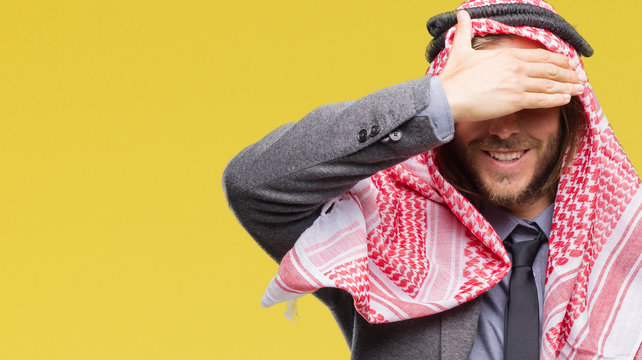 Young handsome arabian man with long hair wearing keffiyeh over isolated background smiling and laughing with hand on face covering eyes for surprise. Blind concept.