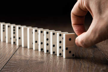Creative background, Male hand pushing white dominoes, on a brown wooden background. Concept of domino effect, chain reaction, copy space.
