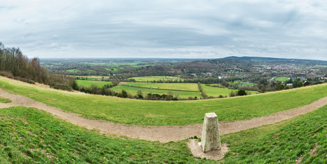 Panorama taken from Box Hill in the Surrey Hills, England, UK, with a trig point in the foreground and farms, fields, the town of Dorking and the village of Brockham in the background. - obrazy, fototapety, plakaty