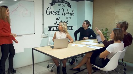 Diverse businesspeople meeting brainstorming team. Girl in red shirt presenting successful strategy in boardroom drawing a graph on a white board hanging on the wall of the office