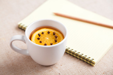 A Cup of tea with a piece of orange and cloves next to a pencil and a notebook on a table covered with a linen tablecloth, write down the list of actions. Concept of planning. Top view, copy space