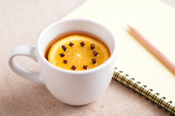 A Cup of tea with a piece of orange and cloves next to a pencil and a notebook on a table covered with a linen tablecloth, write down the list of actions. Concept of planning. Top view, copy space