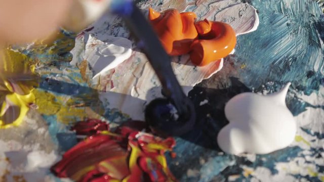 Senior man paints a picture on the beach. Close-up of male artist's hands squeezing the paint from the tube onto the palette.