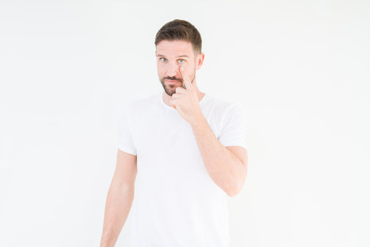 Young handsome man wearing casual white t-shirt over isolated background Pointing to the eye watching you gesture, suspicious expression