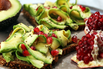sliced avocado and ripe pomegranates on toast bread with spices and avocado.