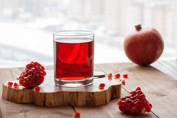 A glass of healthy organic red fruit fresh pomegranate juice and sliced pomegranate on the rustic wood table near to the window sill surface on the white winter city background with a copy space. 