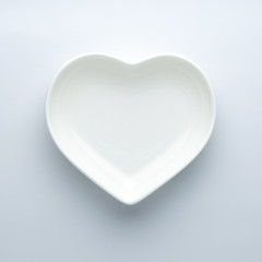 Minimalism. Empty plate in the shape of a heart on a white background in the center of the frame. Modern ceramic glossy dishes. Concept of Valentine's Day or wedding romantic theme. Square. Copyspace.
