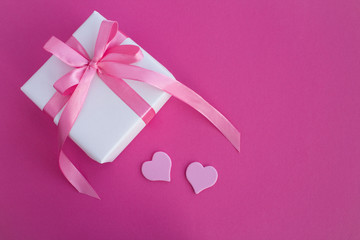 Gift with pink bow and hearts on the dark pink  background.Top view.Copy space.Closeup.