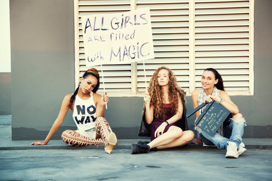 The girls are sitting on the street with a poster. International Womens Day. Women different nationalities,cultures and gender identity. Struggle for freedom, independence, equality