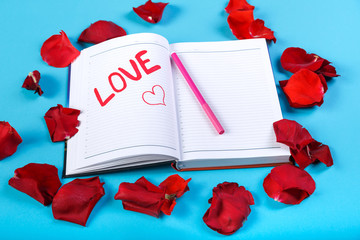 The word love written in red felt-tip pen in a notebook on a blue background in the design of rose petals.