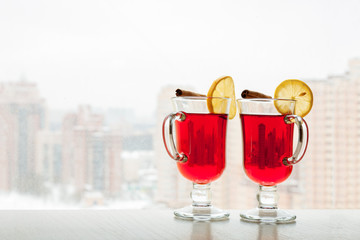Two red hot mulled wine glasses on the window sill surface new building with white winter cityscape background copy space. Selective focus