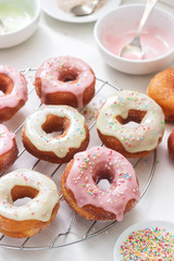 Homemade donuts decorated with colored icing and colored sugar on a light background.