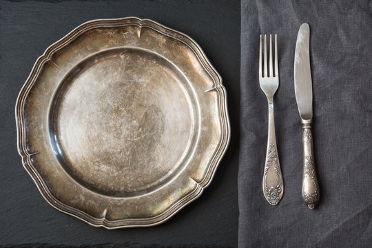 Empty metal dish with knife and fork on slate background, with copy space. Table setting.