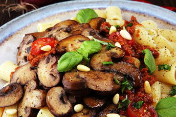 Penne pasta rigatoni in tomato sauce with mushrooms, tomatoes decorated with parsley and basil